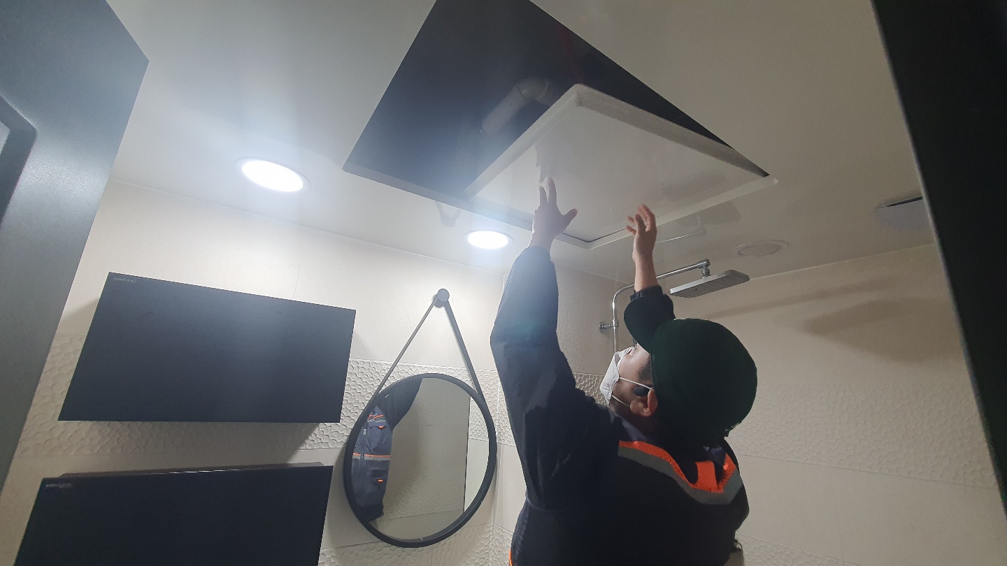 마스크와 모자를 착용한 작업자가 천장 점검구를 열어 내부 배관 상태를 육안으로 확인하고 있습니다.